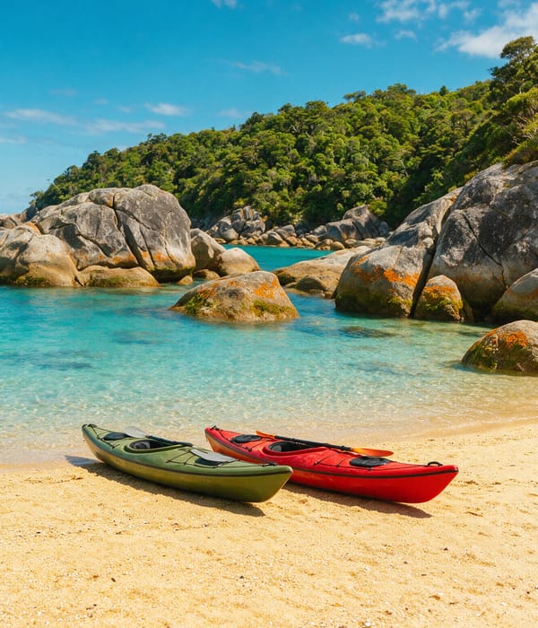 Two sea kayaks on golden sand in an Abel Tasman cove with clear turquoise shallows