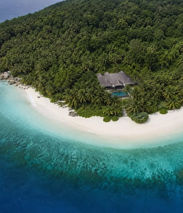 An aerial view of a single villa above a white beach on a private island