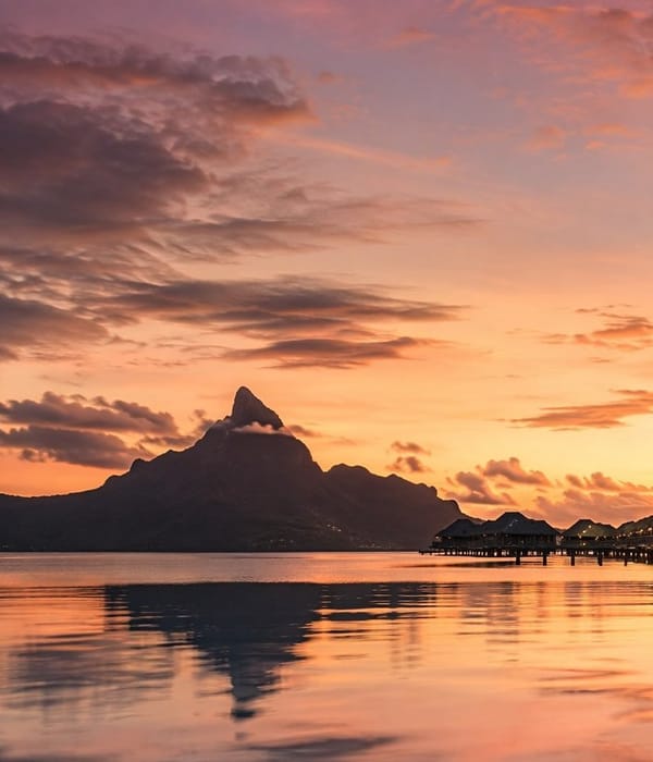 Overwater villas below the silhouette of Mount Otemanu at sunset in Bora Bora