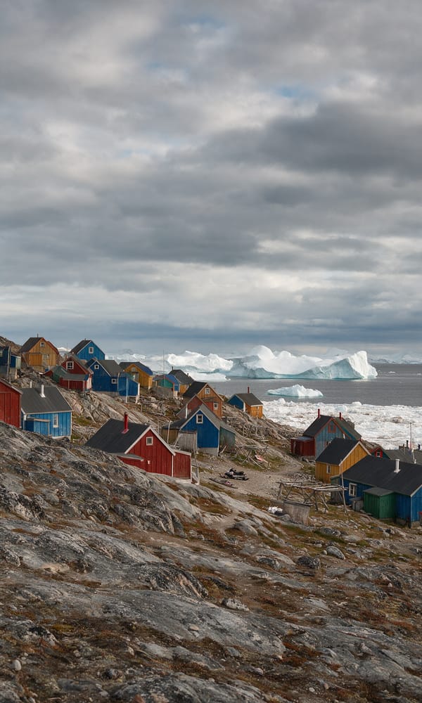 Red, blue and ochre wooden houses scattered up a bare slope above drift ice at Ittoqqortoormiit