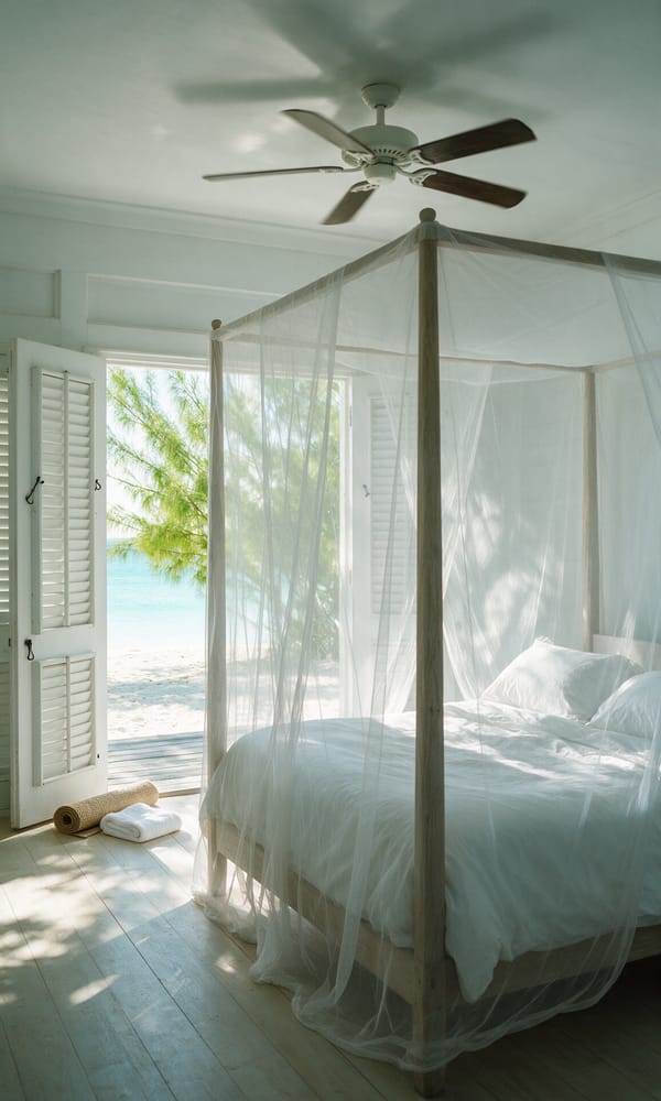A white four-poster bed and open louvered doors framing casuarinas and sea in a Parrot Cay cottage