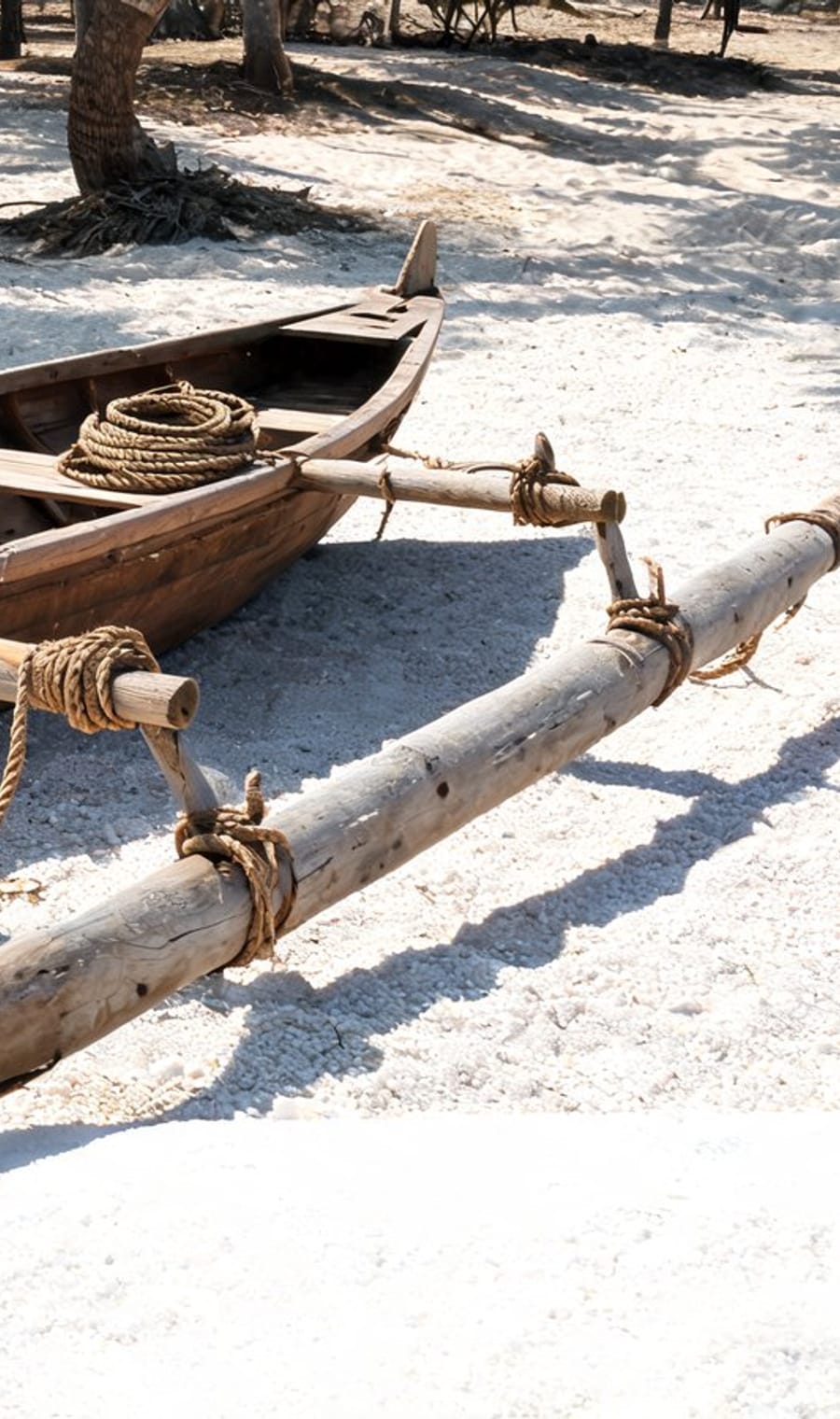 An outrigger canoe pulled up on white sand beside the Aitutaki lagoon
