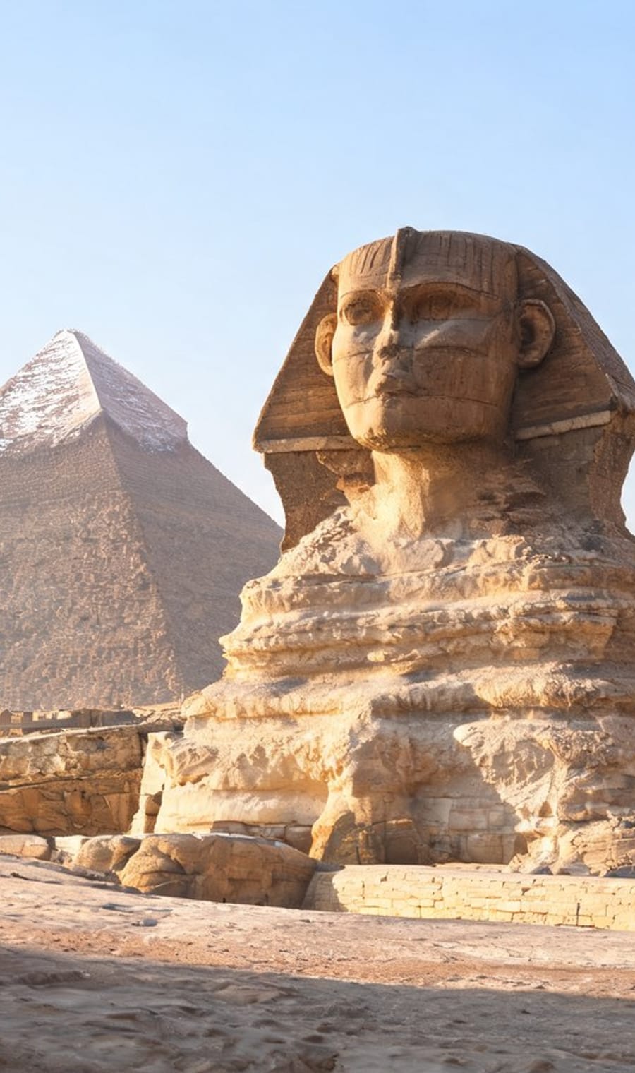 The Great Sphinx with a pyramid of Giza behind it in warm haze