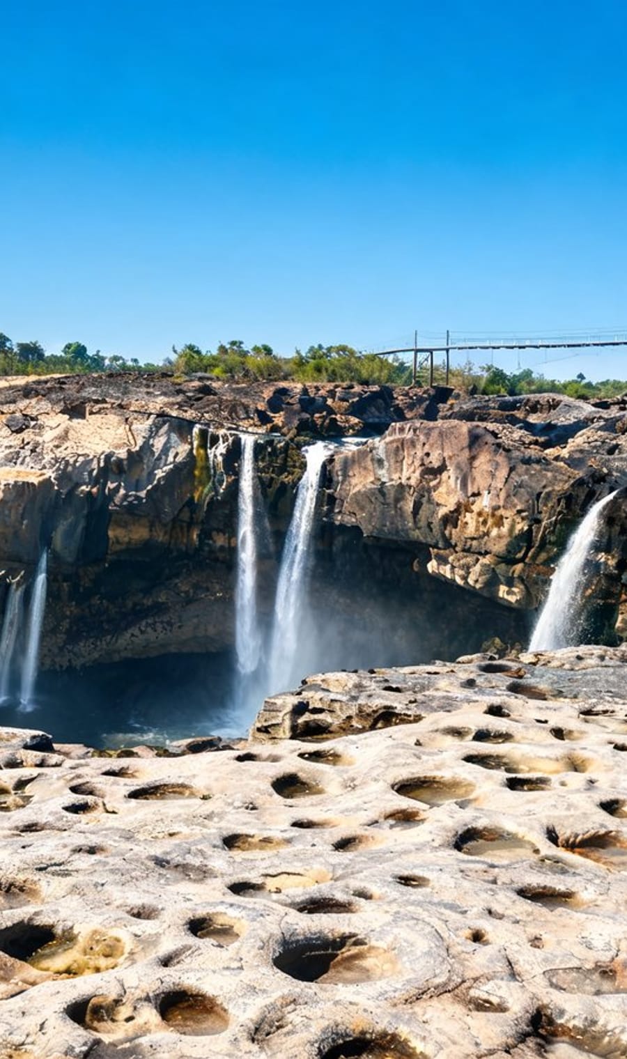 Water pouring over the lip of Victoria Falls beside the pitted rock shelf